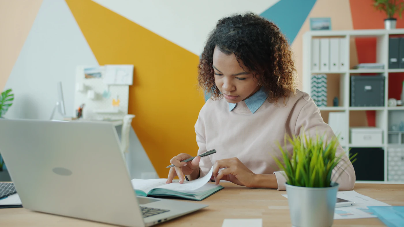A woman reviewing paperwork beside her laptop